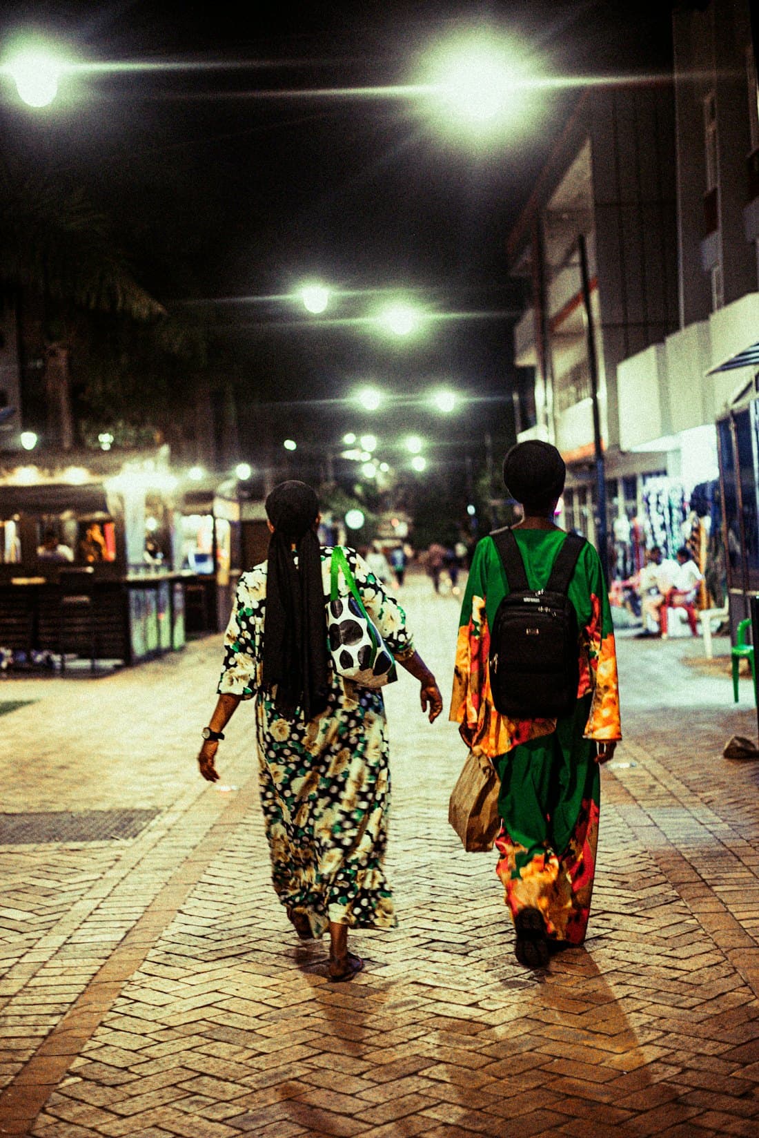 People walking a lamp-lit city street in the evening.